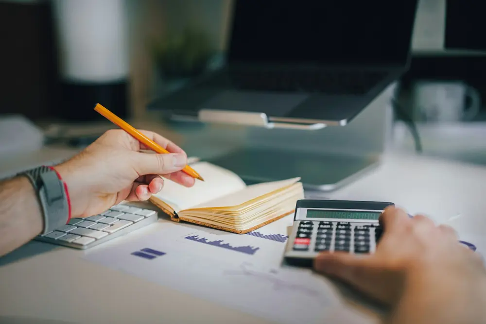 Mani che usano una calcolatrice accanto a un registro dei conti